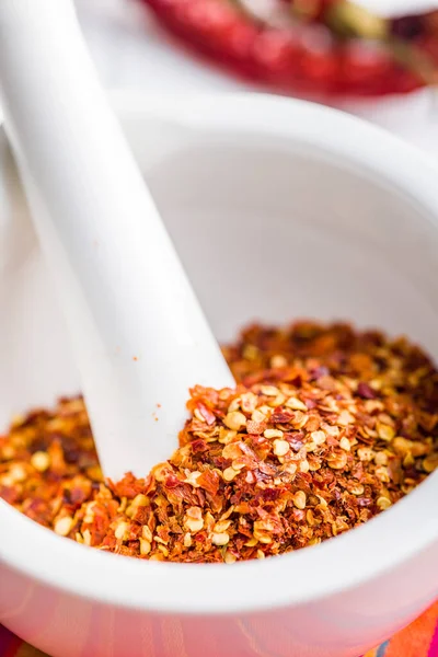 Dry chili pepper flakes. Crushed red peppers in mortar on the white table.