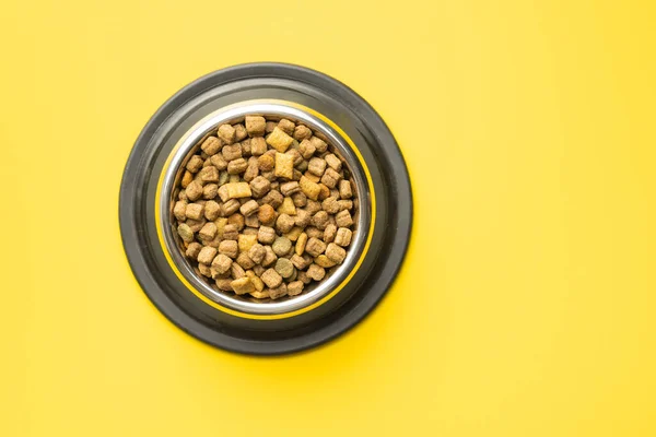 干巴巴地吃宠物食品 狗或猫的食物在黄色背景的碗里 顶部视图 — 图库照片