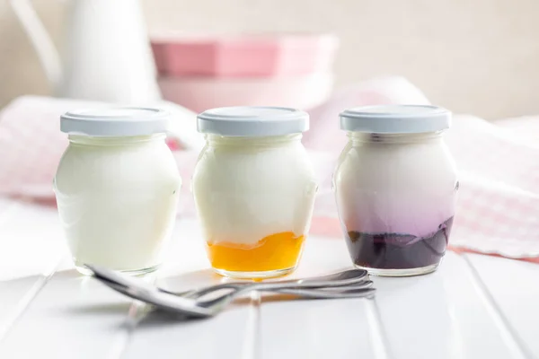 在白桌子上的罐子里放着白色和果味的酸奶 — 图库照片