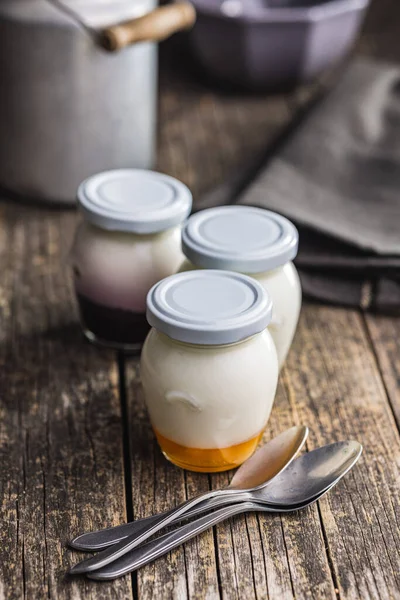 在木制桌子上的罐子里放着白色和水果酸奶 — 图库照片