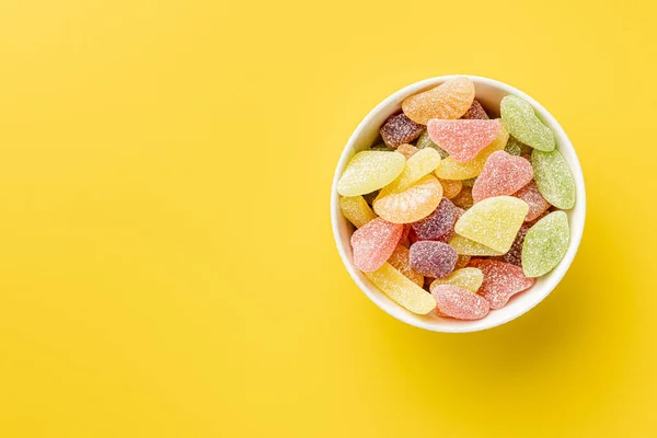 Mix of fruity jelly candy in bowl on the yellow background. Top view.