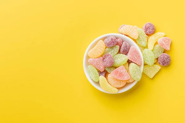 Mix of fruity jelly candy in bowl on the yellow background. Top view.