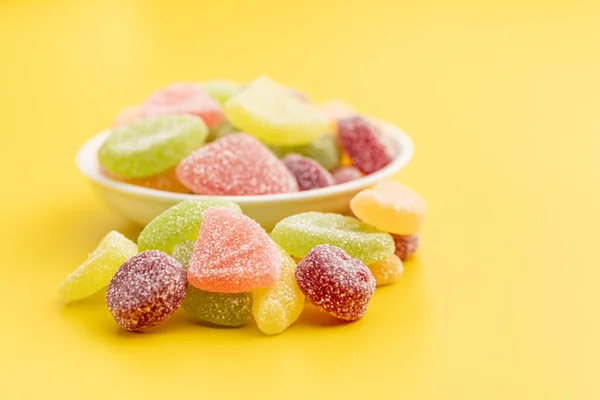 Mix of fruity jelly candy in bowl on the yellow background.