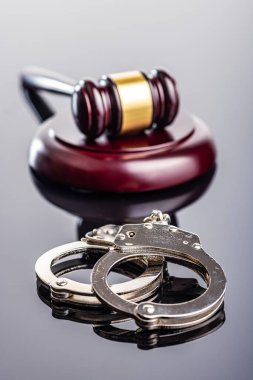 Handcuffs and judge gavel on the mirror table. clipart