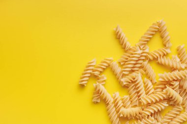 Uncooked fusilli pasta. Uncooked italian pasta on the yellow background. clipart