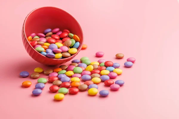 Colorful sweet candies in bowl on the pink background.