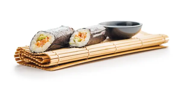 ボウル醤油の横にきちんと置かれた2本の寿司ロールを特徴とする竹製マット 寿司ロールは米 さまざまな食材で満たされています — ストック写真