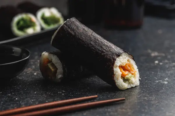 黒いテーブルの上にきちんと置かれた寿司のロールは 使用する準備ができている箸のペアを伴います シンプルさとプレゼンテーションに焦点を当てた新鮮で魅力的な寿司が登場 — ストック写真