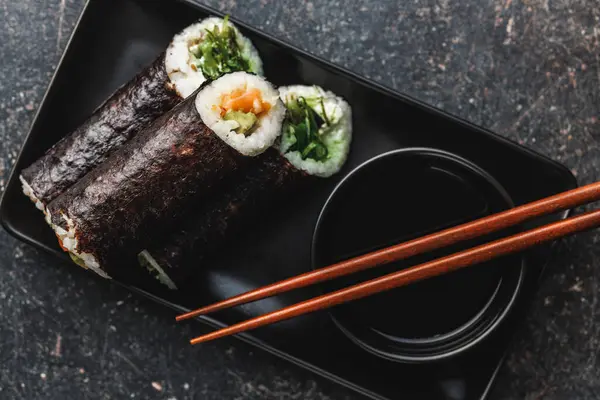 お箸と醤油のボウルを添えた寿司ピース付きのブラックプレート 寿司はさまざまな色 テクスチャ 充填を示し 和食のアーティストリーを紹介しています — ストック写真