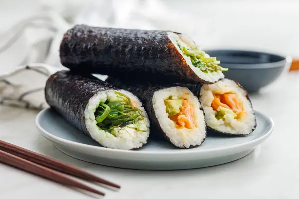 シンプルなキッチンテーブルに置かれた木製の箸と醤油のボウルで さまざまな寿司ロールでいっぱいのプレート — ストック写真