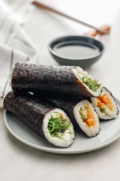 シンプルなキッチンテーブルに置かれた木製の箸と醤油のボウルで さまざまな寿司ロールでいっぱいのプレート — ストック写真