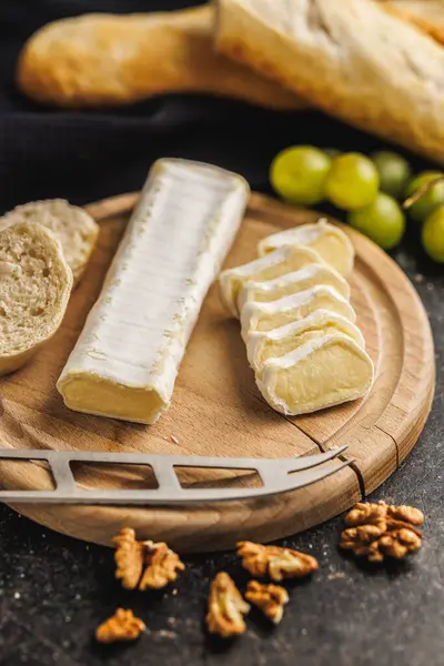 素朴な料理セットアップのための新鮮なフランスパンとブドウを伴う木製チーズボードにスタイリングされたブリーチーズウェッジ ロイヤリティフリーのストック写真