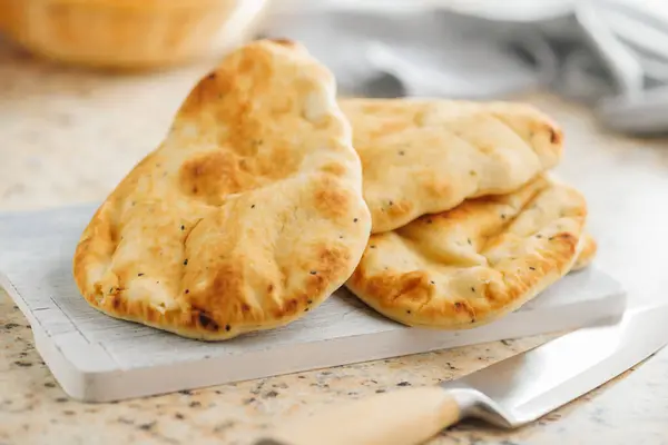 Freshly Baked Naan Bread on citting board on a kitchen table.