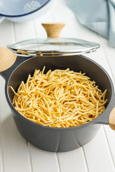 未煮熟的意大利面放在厨房桌子上的锅里 图库图片