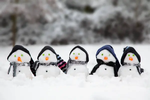 Cute little snowmen in a line dressed in hats and scarfs in winter with a snow background