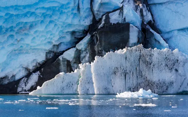 stock image A close-up view of the Jaette glacier with striking blue, black and white ice formations. Icebergs float in the calm fjord water below, in Isfjorden, Northeast Greenland National Park.