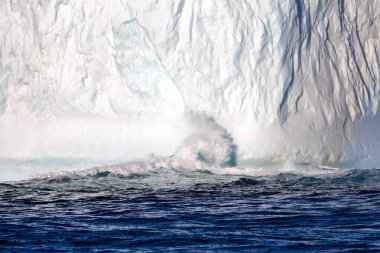 Wave crashes into a huge iceberg in Liverpool Land, Greenland. This is a freshwater iceberg that has calved from a glacier, and then floated out into the open waters of the Arctic Greenland Sea. clipart