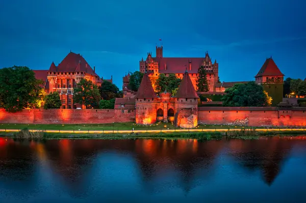 stock image Castle of theTeutonic Order in Malbork by the Nogat river at dusk.