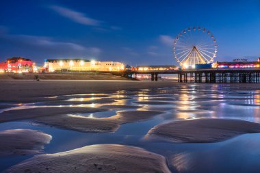 Blackpool, İngiltere - 20 Ekim 2024: Blackpool sahilinde turistik yerleri ve alacakaranlıkta kulesi olan insanlar.