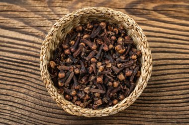 Clove spice in a wicker bowl on a wooden board, Syzygium aromaticum