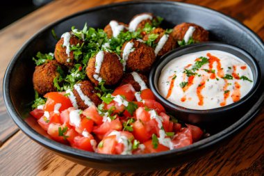 Tahini soslu nefis falafel, domates ve maydanoz ahşap bir masaya konmuş siyah bir kasede servis edilir. Yapay zeka üretken