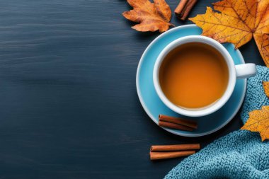 Bir fincan sıcak içecek, tarçın çubukları, sıcak eşarp ve koyu mavi ahşap arka planda renkli akçaağaç yapraklarıyla sonbahar çay saati dinleniyor. Yapay zeka üretken