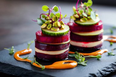 Fıstık, salatalık ve mikroyeşilliklerle süslenmiş pancar ve keçi peyniri Napolyon aperatifi, canlı bir portakal sosuyla birlikte siyah bir tabakta servis ediliyor. Yapay zeka üretken