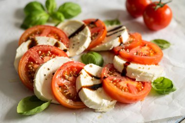 Taze mozzarella ve fesleğen yapraklı domates salatası ve parşömen kağıdına serpiştirilmiş balzamik cila. Yapay zeka üretken