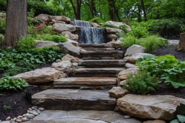 Taştan adımlar, canlı yeşil bir manzaranın ortasında yavaşça çağlayan bir şelaleye doğru yükseliyor ve sakin bir açık hava inzivası yaratıyor. Yapay zeka üretken