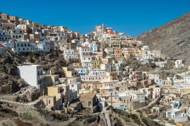 Geleneksel beyazlatılmış renkli aksanlı evler olimpos köyünün dik yamaçlarını kaplayarak açık mavi gökyüzünün altında güzel bir manzara yaratıyor.