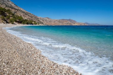 Kristal berrak turkuaz su, engebeli Girit dağları tarafından kucaklanan Apella sahilinin çakıllı sahillerine vuruyor.