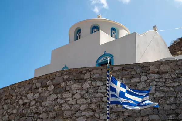 Geleneksel Yunan beyaz ve mavi kilisesi, rüzgarda dalgalanan Yunan bayrağıyla