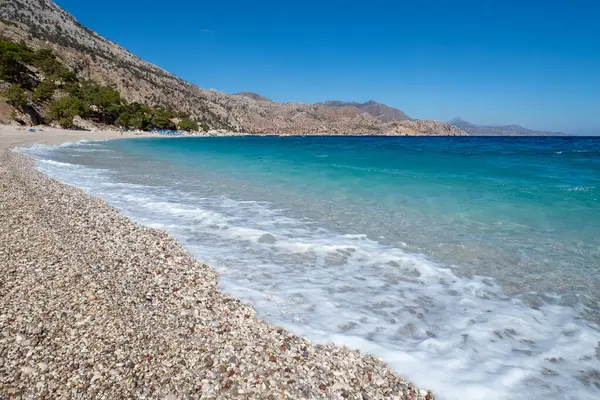 Kristal berrak turkuaz su, engebeli Girit dağları tarafından kucaklanan Apella sahilinin çakıllı sahillerine vuruyor.