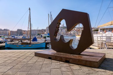 Eski limanın iskelesinde M harfi aşk kilitleri, marinada demirli tekneler ve Fransa 'nın Marsilya tepesinde Notre-Dame de la Garde Bazilikası.
