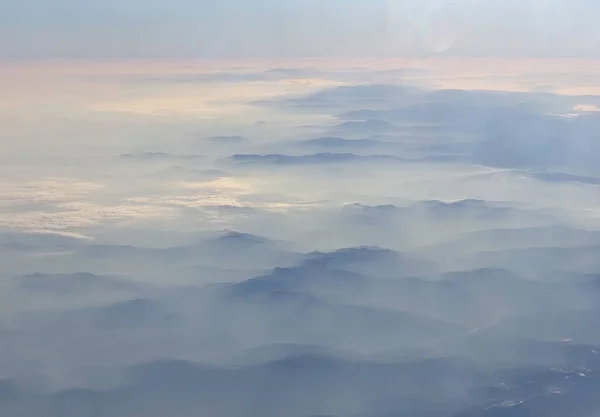 View of the mountains in the fog at dawn from the airplane window. Beautiful wallpaper.