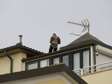  İnşaat işçileri mavi gökyüzüne karşı çatıyı tamir ediyorlar. Roofer evin tepesine kiremit döşedi. Yenilemek, geliştirmek, profesyonel takım çalışması ile evin dışını inşa etmek. Güvenlik, koruma kavramı
