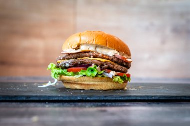 Siyah arka planda susamlı sığır burger, marullu çörek, domates peyniri.