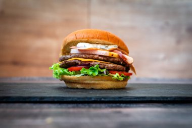 Siyah arka planda susamlı sığır burger, marullu çörek, domates peyniri.