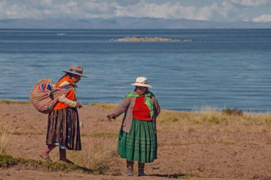 AMANTANI Adaları, PUNO, PERU, - 29 Nisan 2022: Geleneksel kıyafet ve tekstil giymiş iki Quechua yerlisi kadın Taquile Adası 'nda Titicaca Gölü, Puno, Peru' da yürüyen merdivenler.