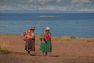 AMANTANI Adaları, PUNO, PERU, - 29 Nisan 2022: Geleneksel kıyafet ve tekstil giymiş iki Quechua yerlisi kadın Taquile Adası 'nda Titicaca Gölü, Puno, Peru' da yürüyen merdivenler.