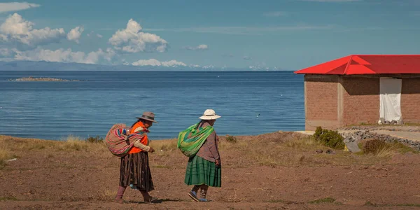 stock image AMANTANI ISLAND, PUNO, PERU, - 29 April 2022: Two Quechua indigenous women in traditional clothing and textile walking down the steps on Taquile island by the Titicaca Lake, Puno, Peru.