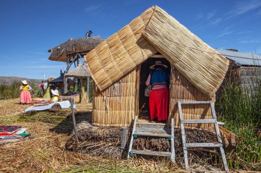 Uros, Peru - 29 Nisan 2022: Peru 'daki Titicaca Gölü' nde yüzen Uros Adaları 'ndaki ev yakınlarında geleneksel elbiseli kadınlar.