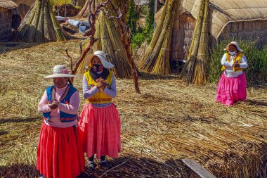 Uros, Peru - 29 Nisan 2022: Peru 'daki Titicaca Gölü' nde yüzen Uros Adaları 'ndaki ev yakınlarında geleneksel elbiseli kadınlar.