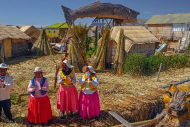 Uros, Peru - 29 Nisan 2022: Peru 'daki Titicaca Gölü' nde yüzen Uros Adaları 'ndaki ev yakınlarında geleneksel elbiseli kadınlar.