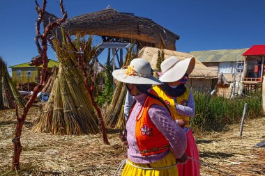 Uros, Peru - 29 Nisan 2022: Peru 'daki Titicaca Gölü' nde yüzen Uros Adaları 'ndaki ev yakınlarında geleneksel elbiseli kadınlar.