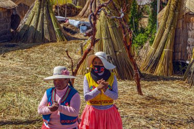 Uros, Peru - 29 Nisan 2022: Peru 'daki Titicaca Gölü' nde yüzen Uros Adaları 'ndaki ev yakınlarında geleneksel elbiseli kadınlar.