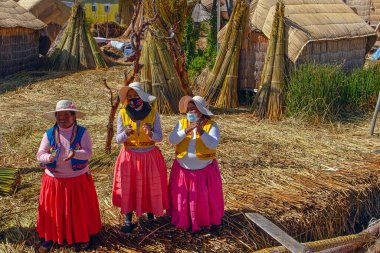 Uros, Peru - 29 Nisan 2022: Peru 'daki Titicaca Gölü' nde yüzen Uros Adaları 'ndaki ev yakınlarında geleneksel elbiseli kadınlar.