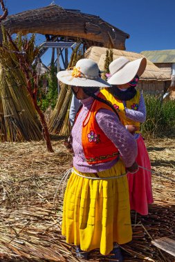 Uros, Peru - 29 Nisan 2022: Peru 'daki Titicaca Gölü' nde yüzen Uros Adaları 'ndaki ev yakınlarında geleneksel elbiseli kadınlar.