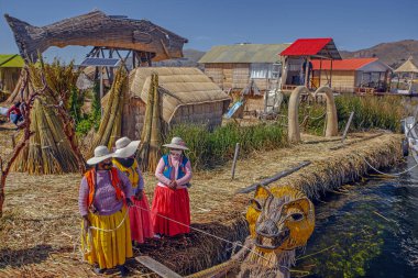 Uros, Peru - 29 Nisan 2022: Peru 'daki Titicaca Gölü' nde yüzen Uros Adaları 'ndaki ev yakınlarında geleneksel elbiseli kadınlar.