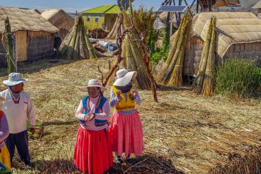 Uros, Peru - 29 Nisan 2022: Peru 'daki Titicaca Gölü' nde yüzen Uros Adaları 'ndaki ev yakınlarında geleneksel elbiseli kadınlar.